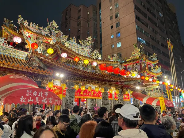 Crowds beneath illuminated red lanterns and ornate temple roofs at night