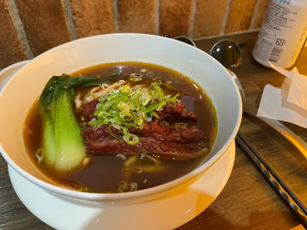 Beef noodle soup with greens in a white bowl