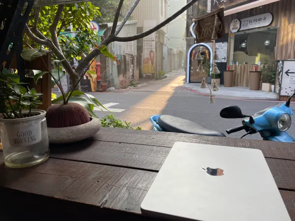 A laptop beside an open café window overlooking a sunlit lane